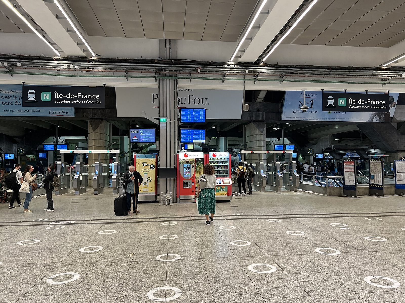 Vestibylen på Gare Montparnasse med billettsperrer, avgangstavler og reisende med koffert