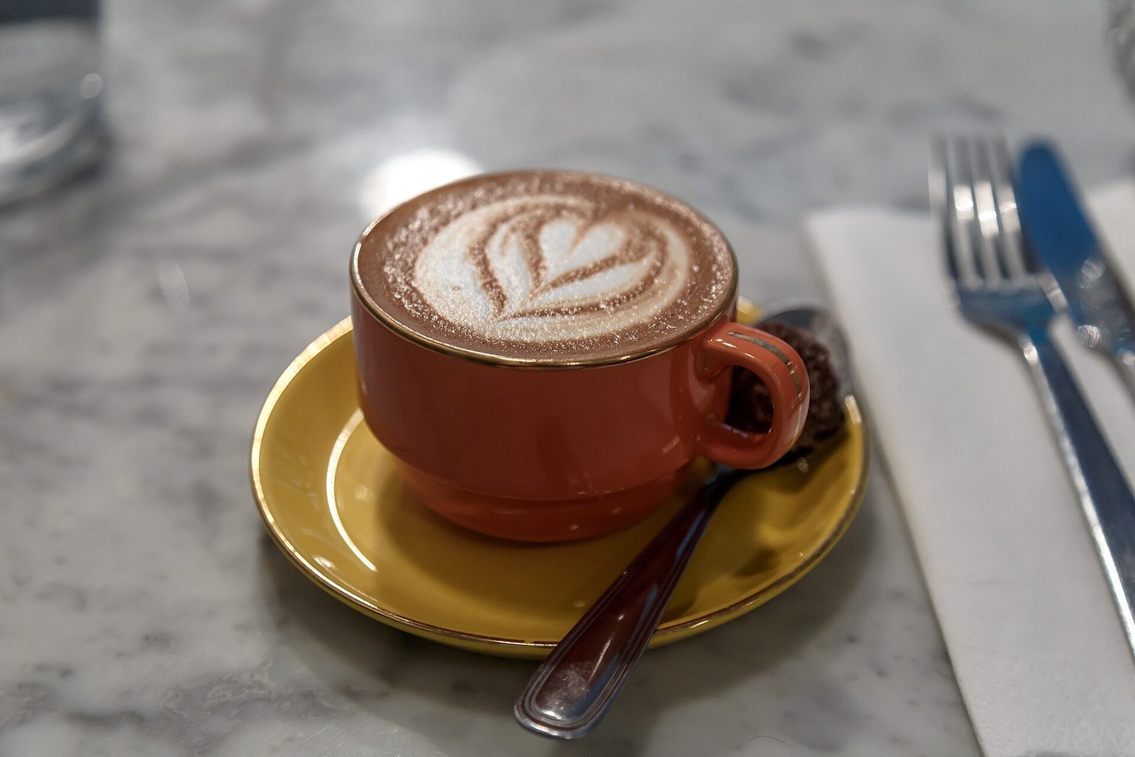 Cappuccino med melkeskum-mønster i rød kopp på gul skål