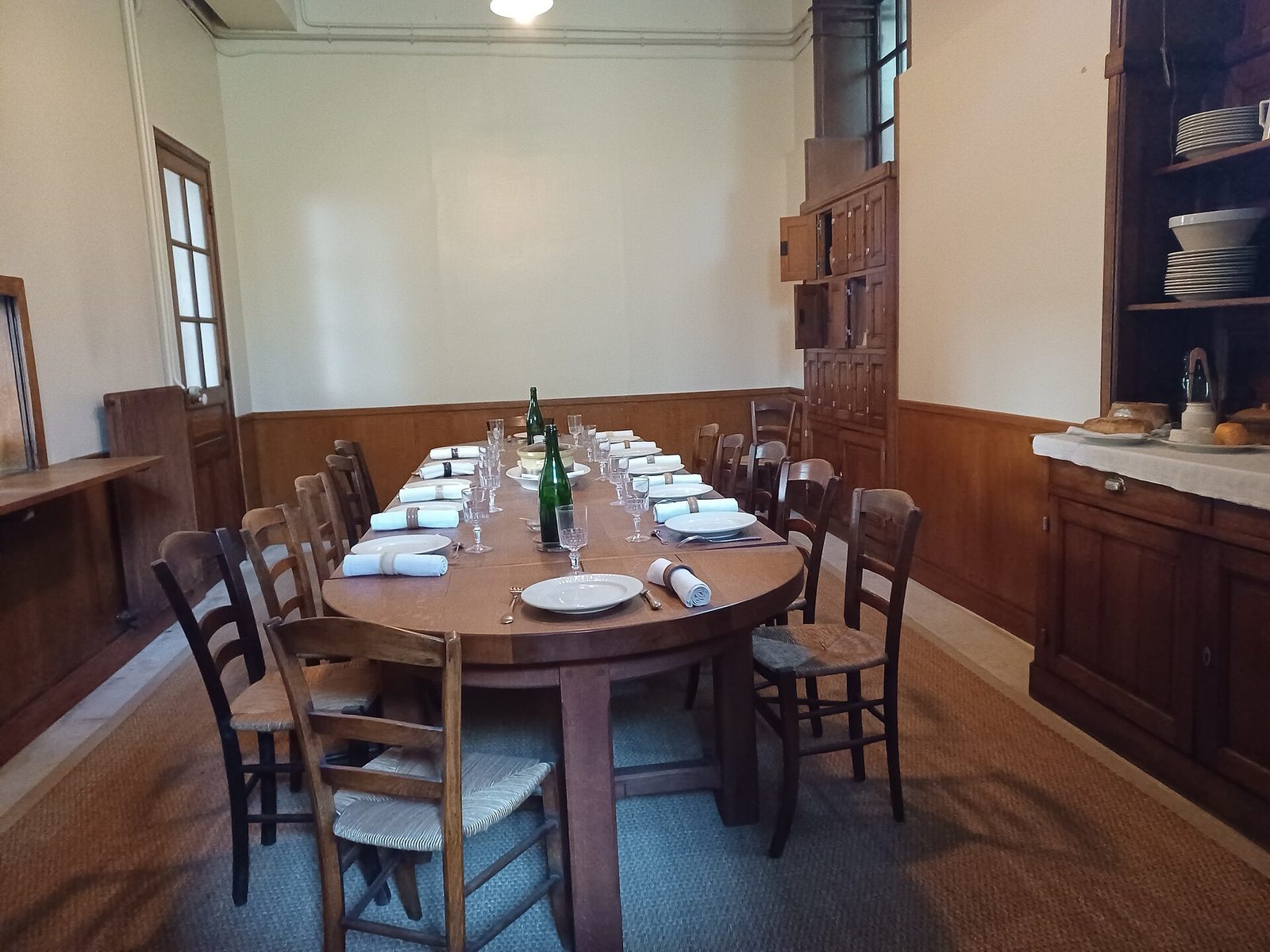 Tjenerskapets spisestue i Camondo-huset, med langbord, enkle stoler og trepaneler