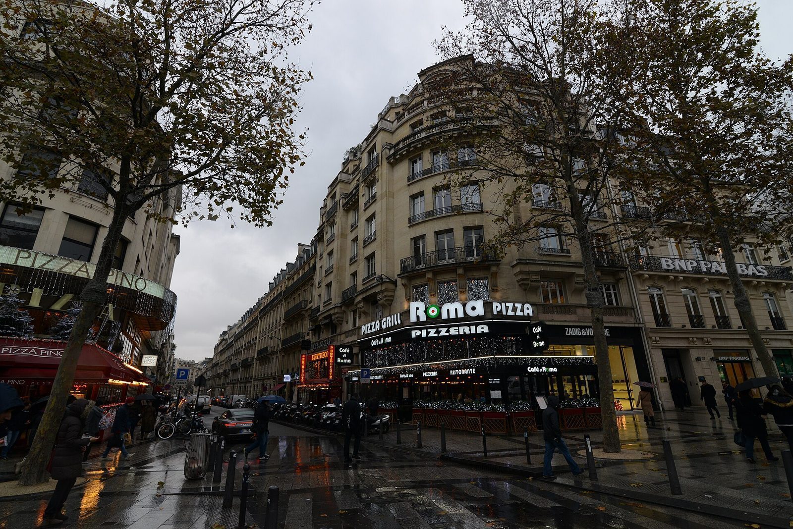 Hjørne på Champs-Élysées i regnvær med opplyste butikk- og restaurantskilt