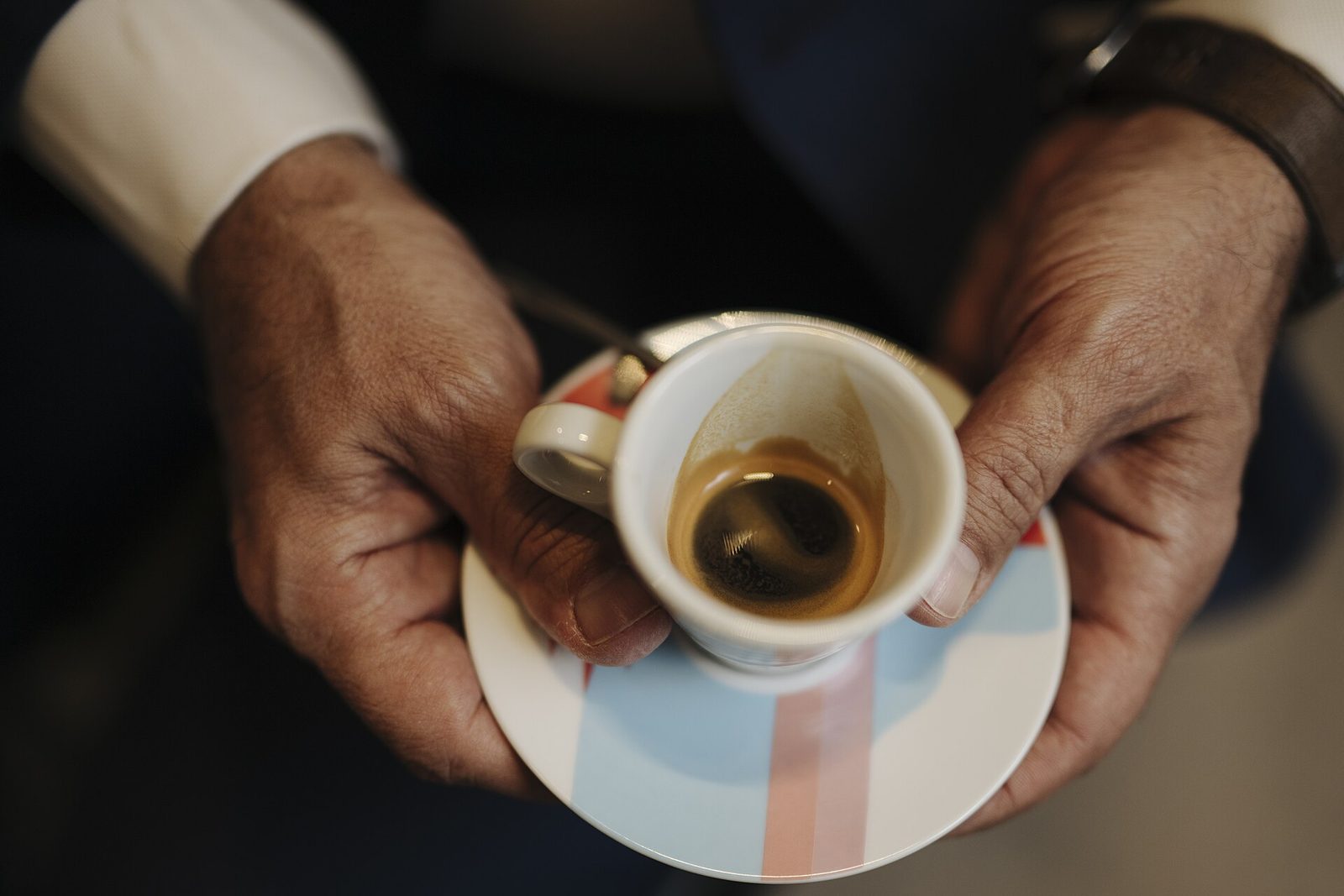 Hender som holder en liten espressokopp på en asjett