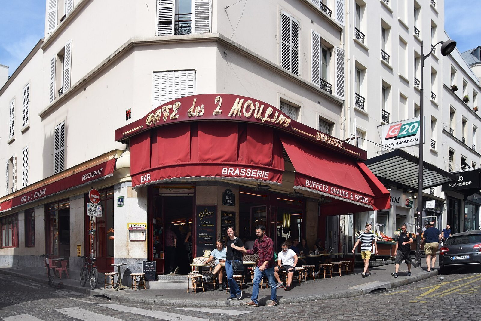 Hjørnefasaden til Café des 2 Moulins i Rue Lepic med rødt markiseskilt og uteservering