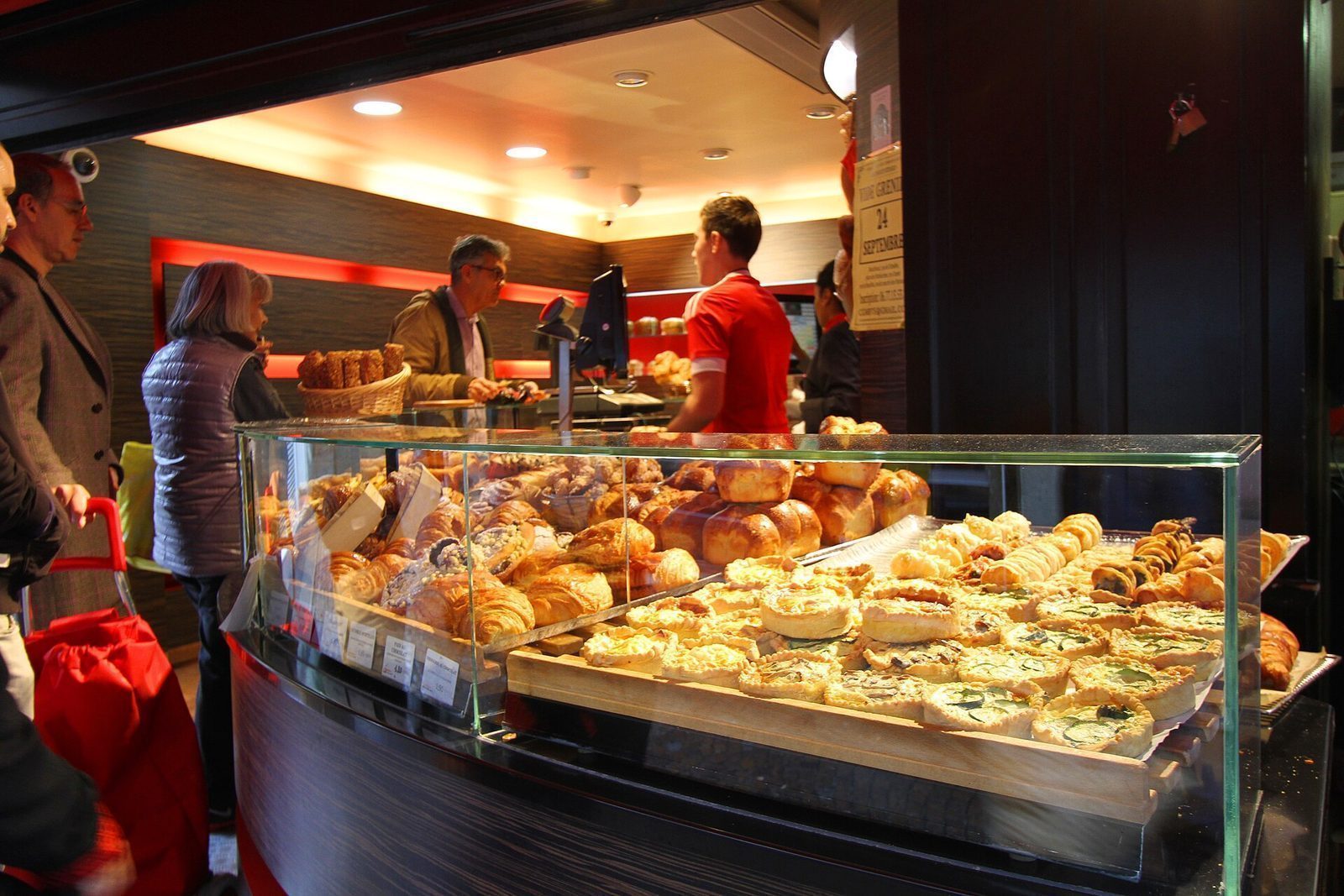 Disk i et parisisk bakeri fylt med croissanter, brioche og quiche, med kunder som blir ekspedert
