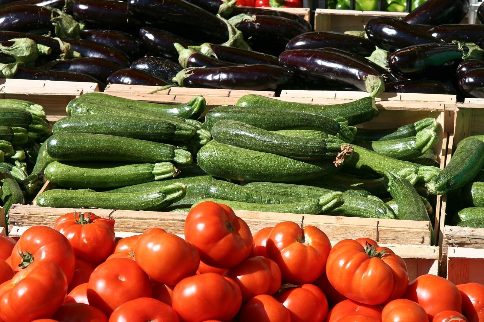 Kasser med auberginer, squash og tomater på en fransk markedsbod
