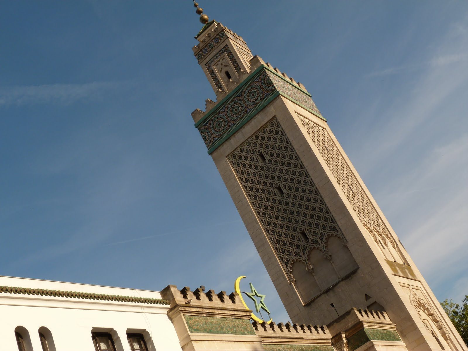 Minaretet på Grande Mosquée de Paris med mosaikkbånd og gjennombrutt steindekor mot blå himmel