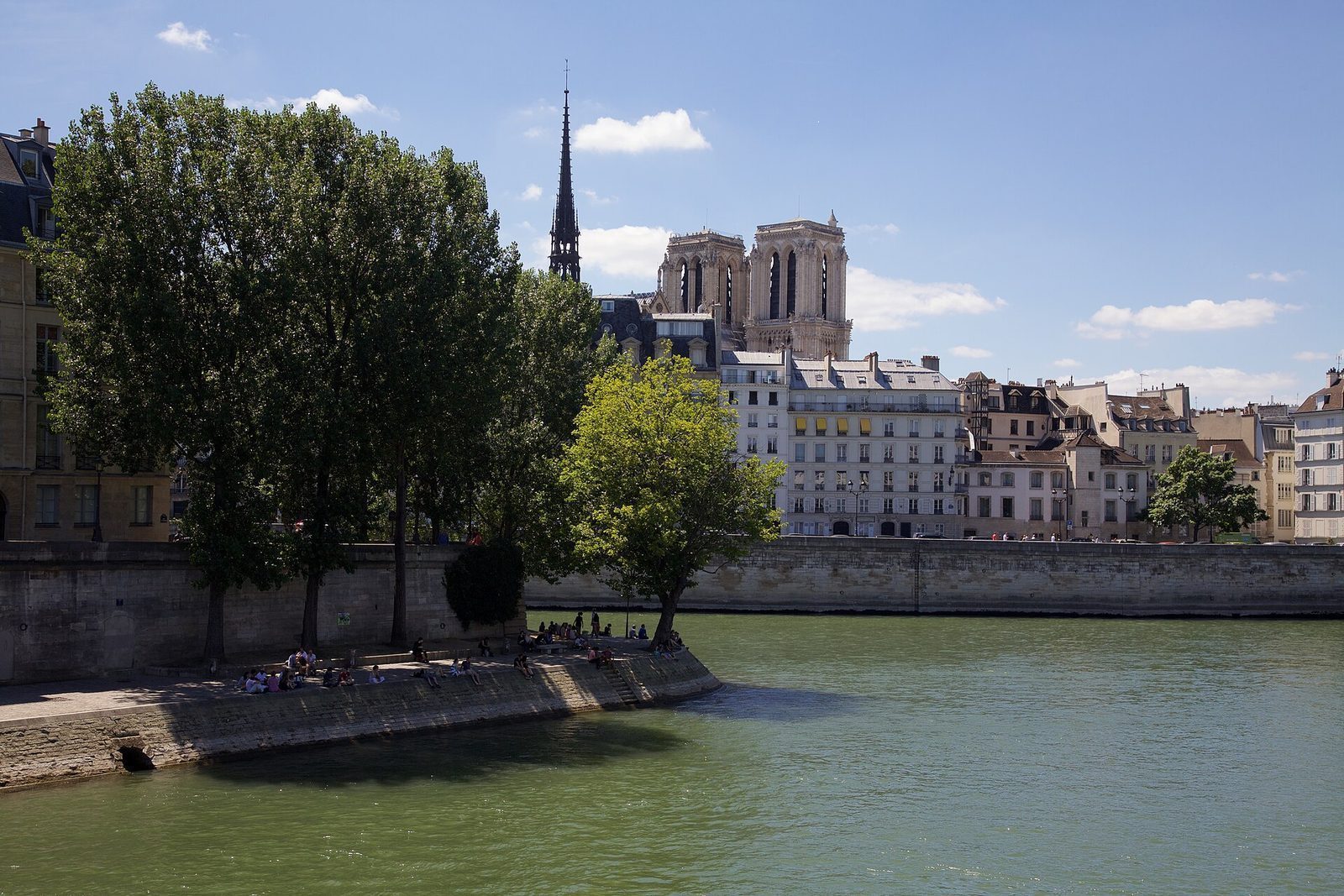 Kaien pa Ile Saint-Louis med folk i solen og Notre-Dames tarn og spir bak