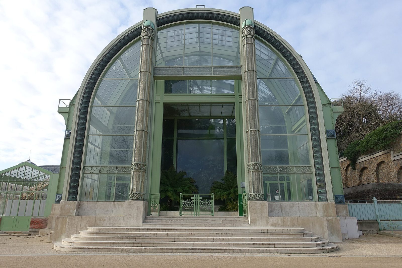 Den store buede glassbygningen i Jardin des Plantes, med bregner og palmer synlige innenfor rutene