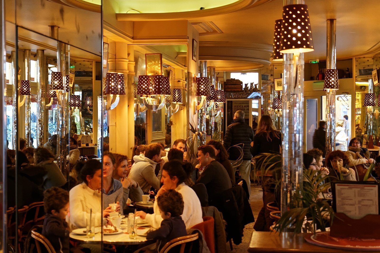 Fullsatt parisisk kafé innvendig med speilvegger, lampetter og gjester ved små runde bord
