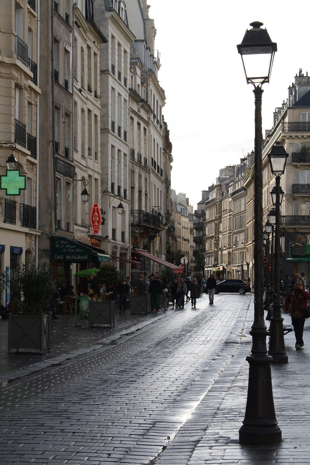 Rue François Miron i Marais med gatelykter, apotekkors, kaféfortau og fotgjengere på våt brostein