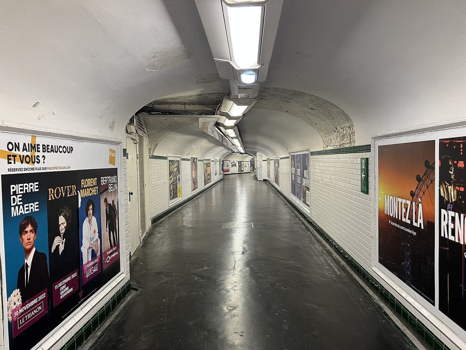 Tom, hvitflislagt gangkorridor i Paris-metroen med buet tak og reklameplakater langs veggene