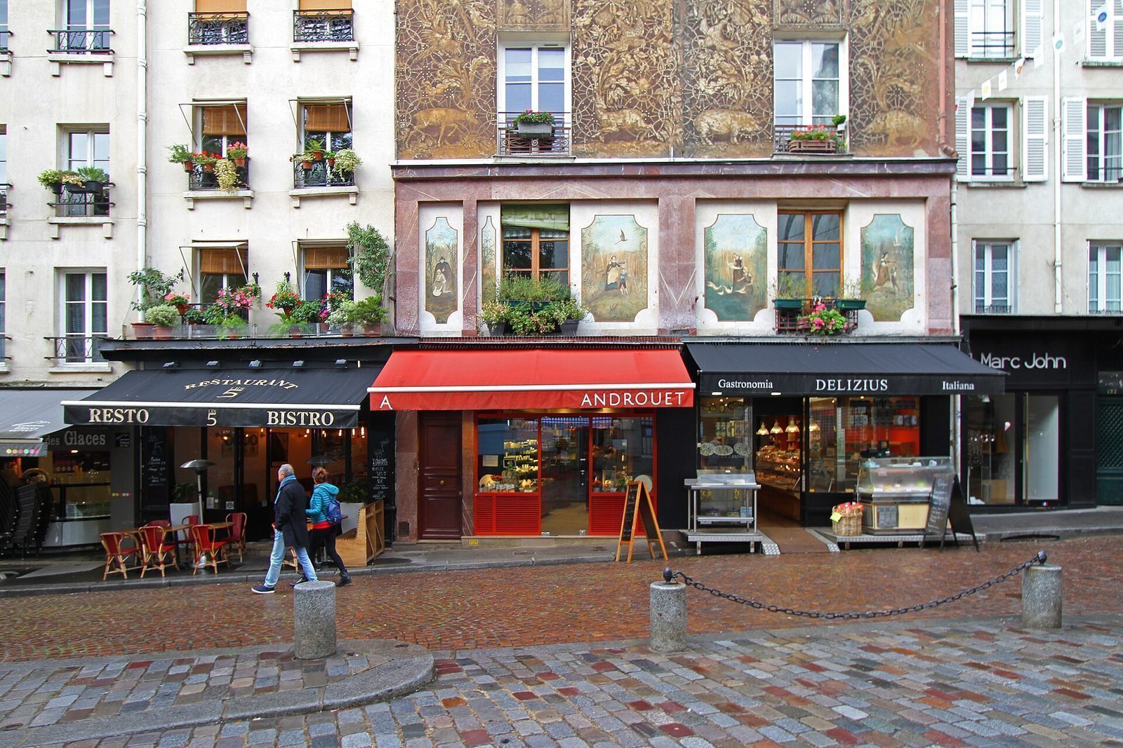 Bistro, ostebutikk og delikatesseforretning under en bemalt husvegg nederst i Rue Mouffetard