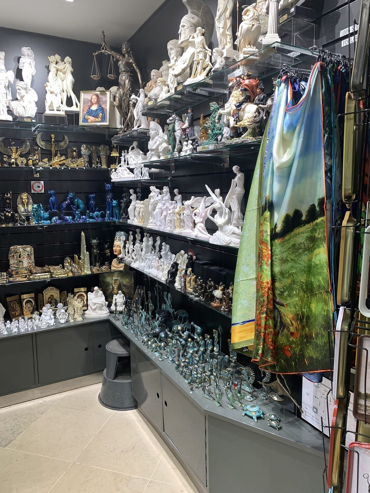 Hyller med gipsfigurer, kunstkopier og silkeskjerf i en butikk under Louvre
