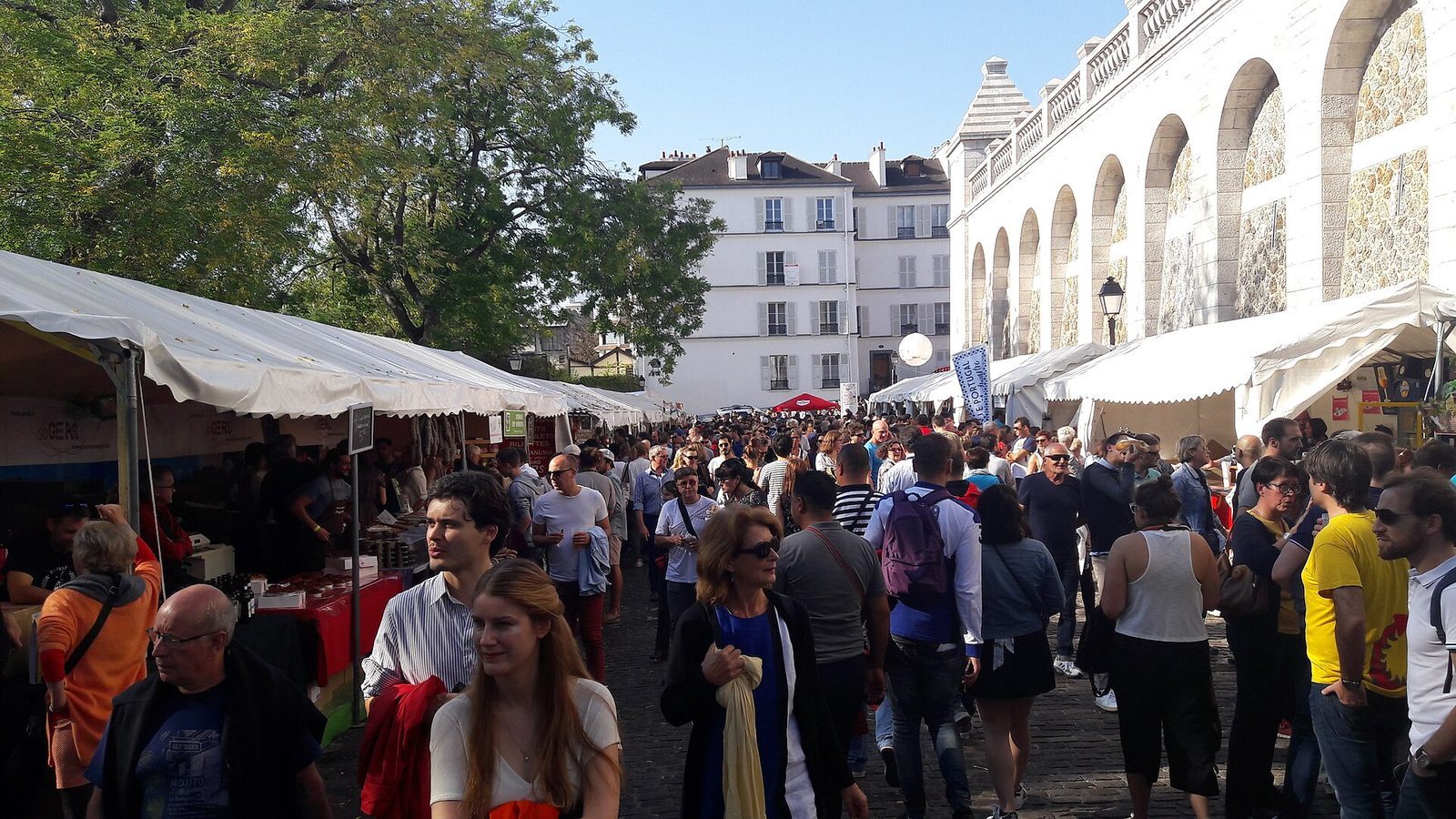 Tett folkemengde mellom hvite salgsboder i en brosteinsgate på Montmartre under vinhøstfesten