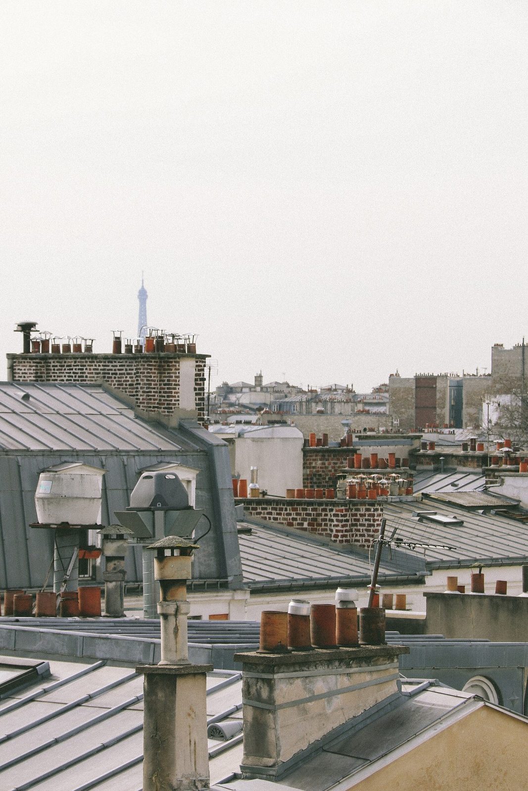 Nærbilde av parisiske sinktak med rader av teglrøde skorsteinspiper og Eiffeltårnet svakt i det fjerne