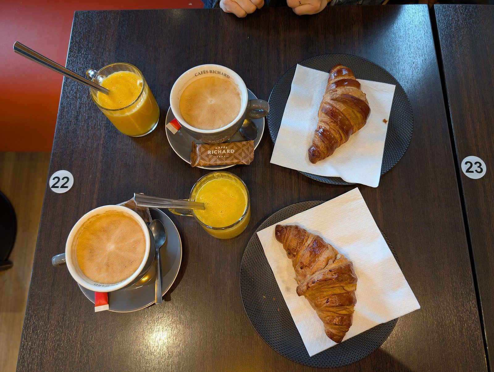 Fransk hotellfrokost sett ovenfra: café crème, appelsinjuice og croissanter på et mørkt bord