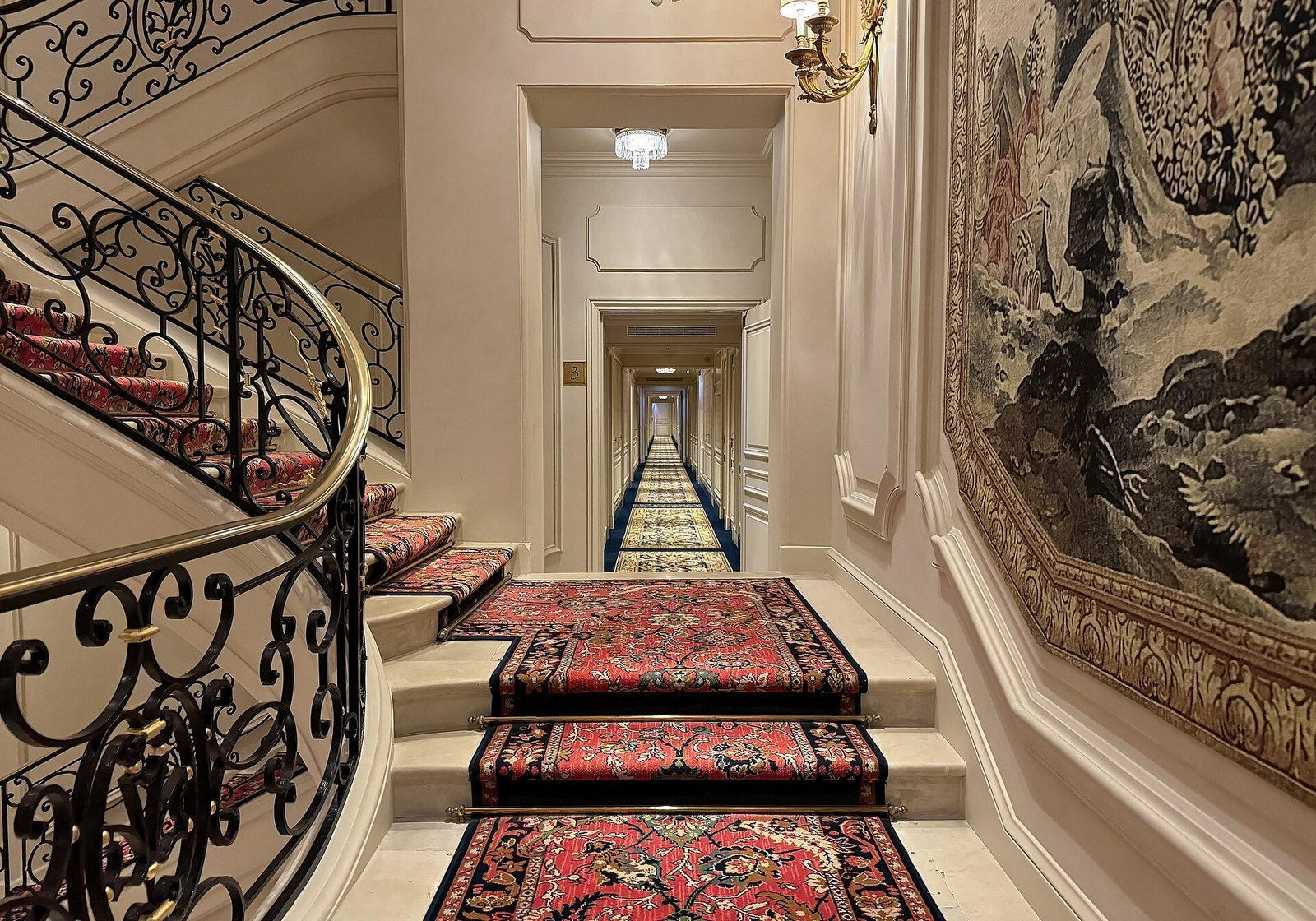 Korridor og trapp inne på Ritz Paris med veggteppe, smijernsrekkverk og mønstrede løpere