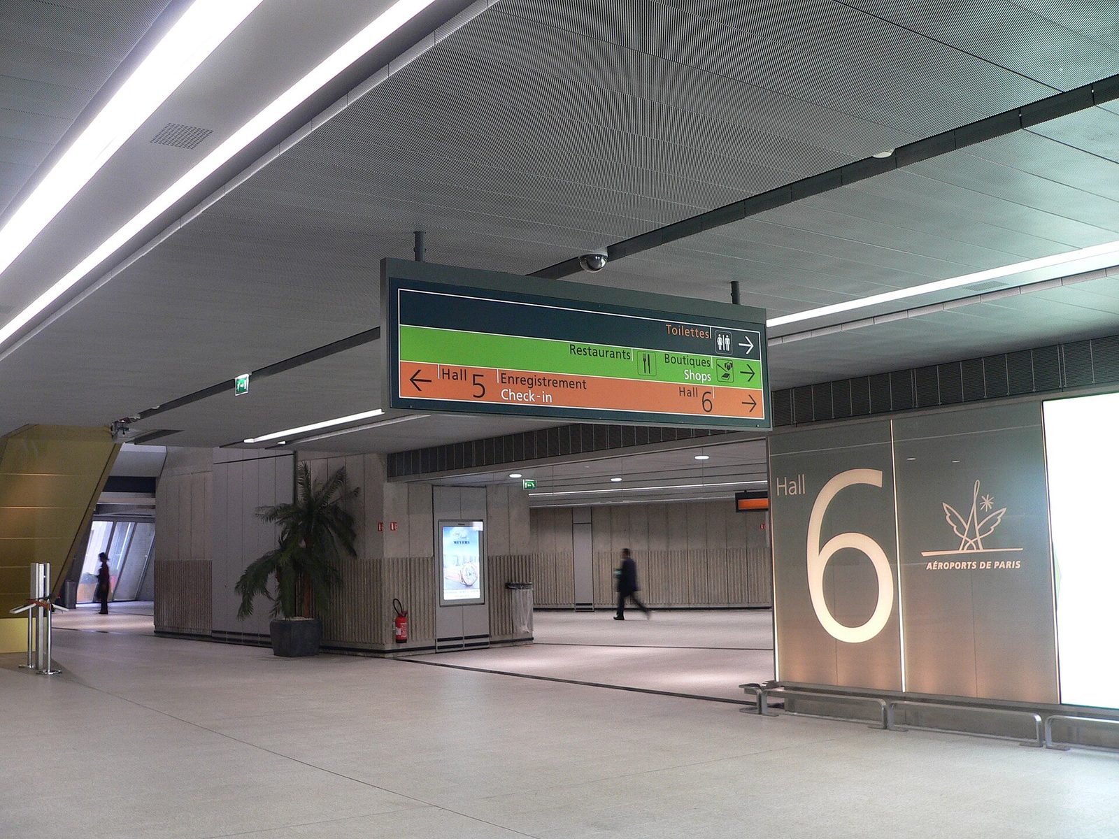 Tospråklig skilting til innsjekk og haller i Terminal 1 på Charles de Gaulle, med en enkelt reisende i bakgrunnen