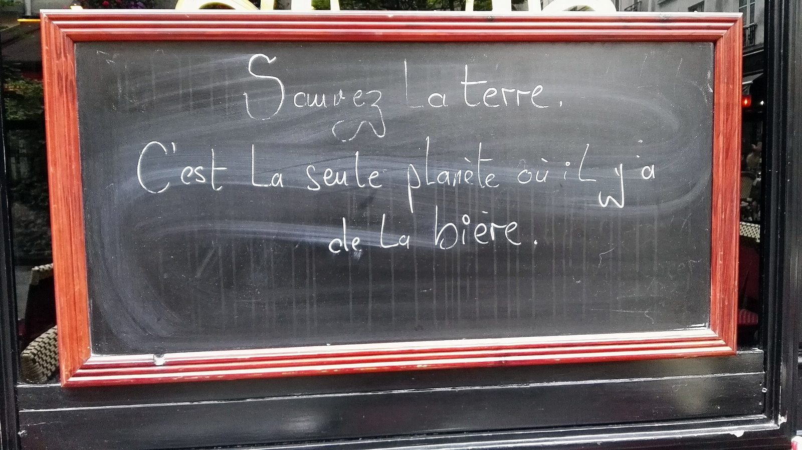 Krittavle med rød ramme utenfor en parisisk kafé med håndskrevet fransk tekst