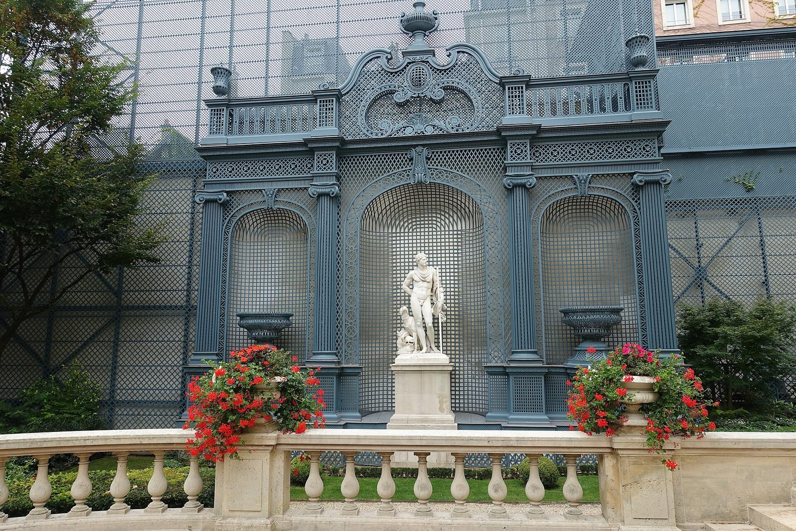 Blåmalt espalierpaviljong med marmorstatue og røde pelargoniaer i hagen ved Hôtel de Matignon