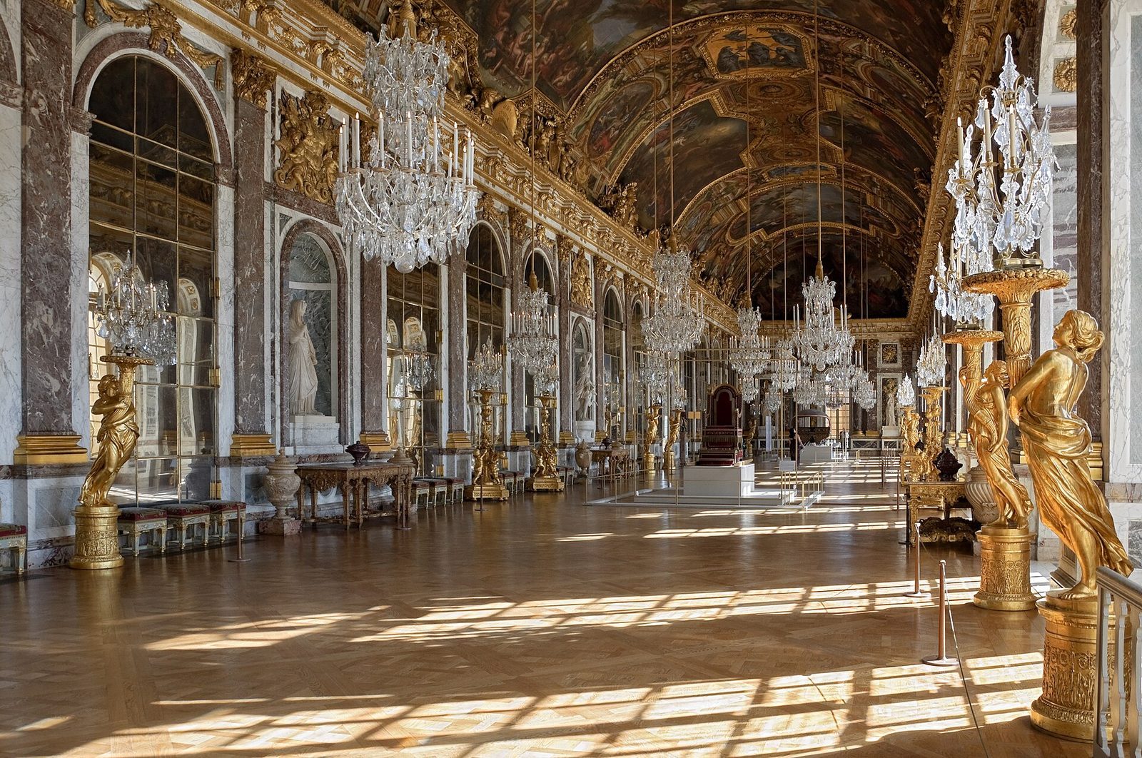 Speilsalen i Versailles med krystallysekroner, forgylte kandelabre og sollys over parkettgulvet