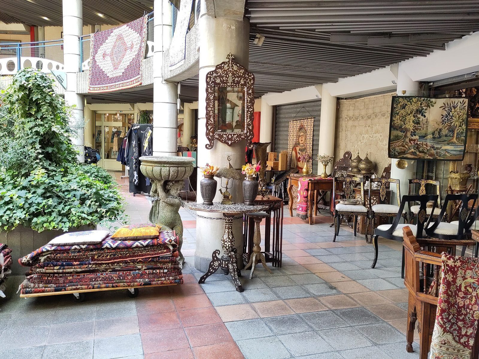 Overbygd markedsgalleri i Saint-Ouen med tepper, speil, møbler og stoler stilt ut langs gangen