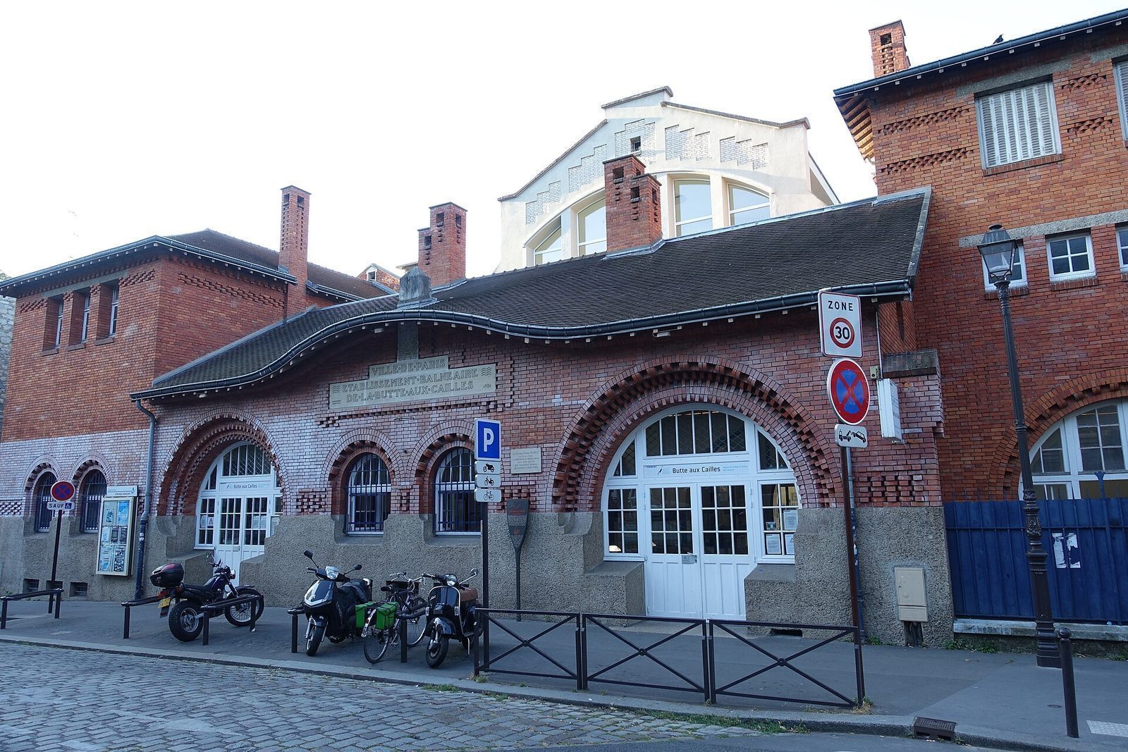 Den fredede teglfasaden til Piscine de la Butte-aux-Cailles med buede vinduer og innhugget navnetrekk