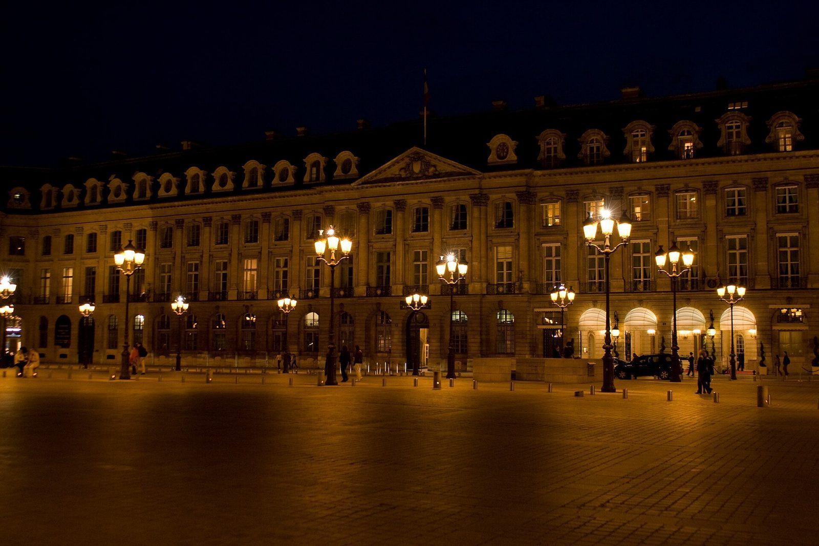 Fasadene rundt Place Vendôme opplyst av gatelykter en kveld, med arkadene til Hôtel Ritz til høyre
