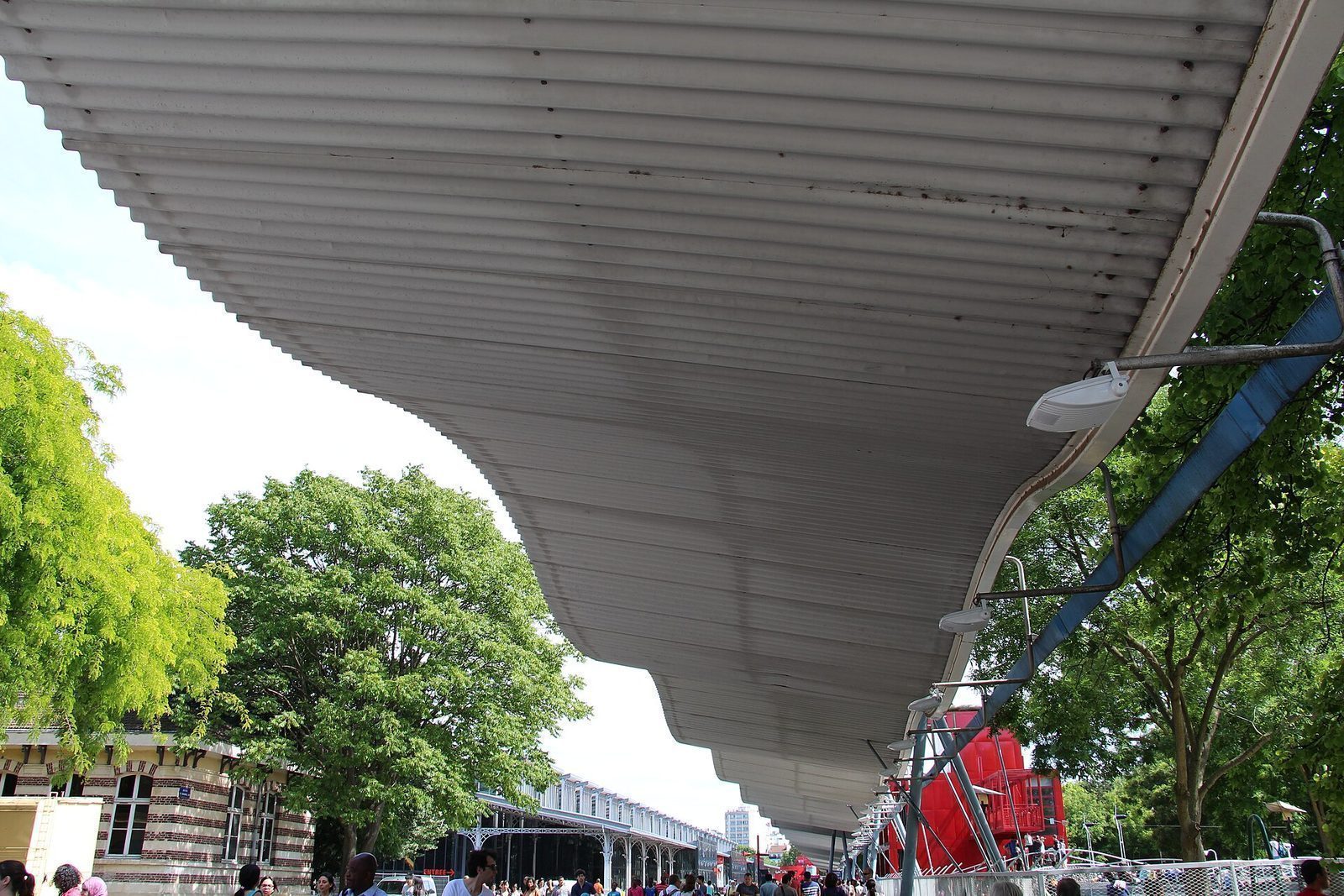 Den bølgende overbygde promenaden i Parc de la Villette, med en rød folie og Grande Halle bak
