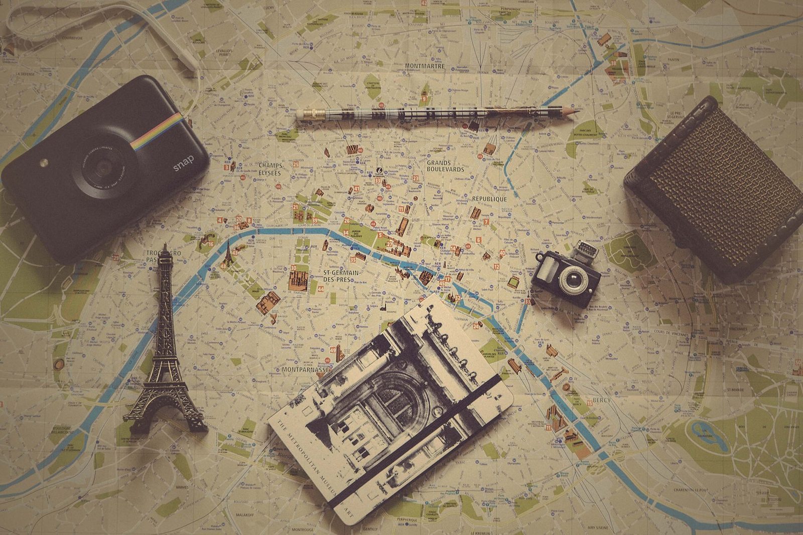 Papirkart over Paris med arrondissementer og landemerker, med kamera, notatbok, blyant og en liten Eiffeltårn-figur oppå